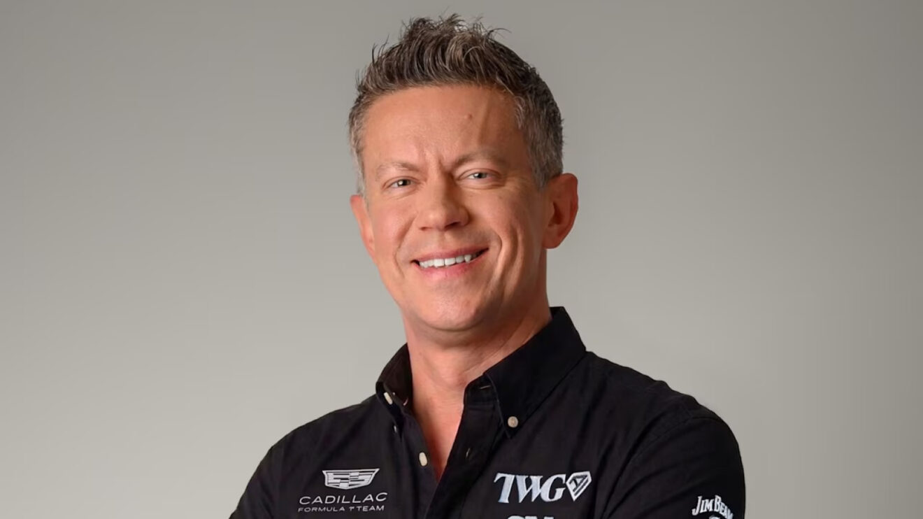 Marcin Budkowski smiles while wearing a black Cadillac team shirt against a grey background